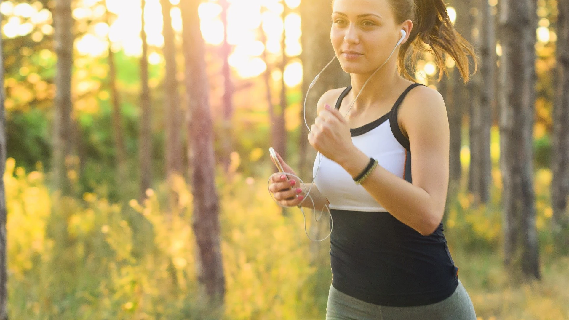 Chica corre por el bosque mientras escucha música en su teléfono móvil