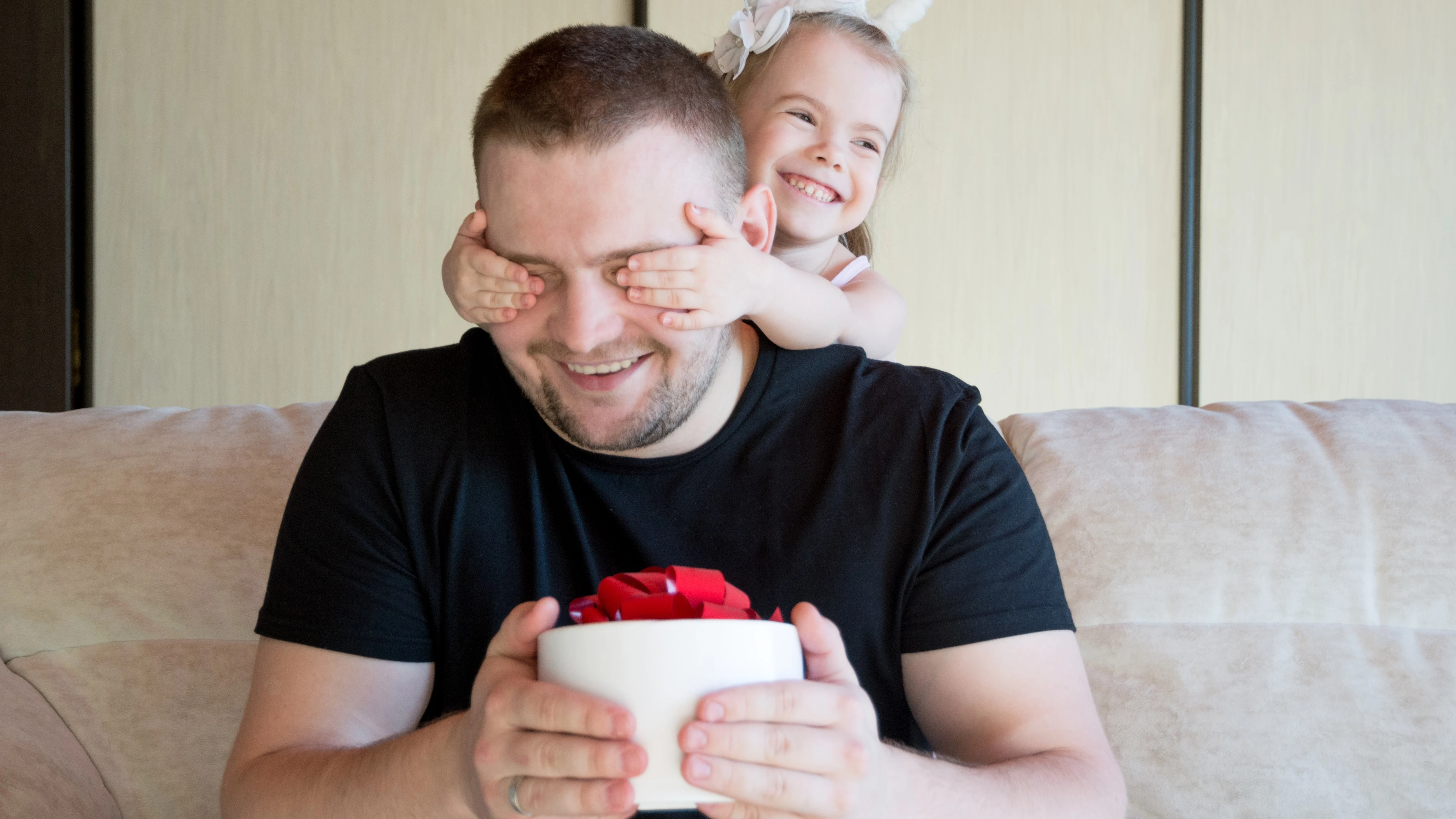 Niña pequeña tapa los ojos a su padre al darle un regalo 