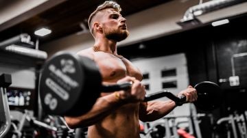 Un hombre entrena en un gimnasio con una barra de pesas