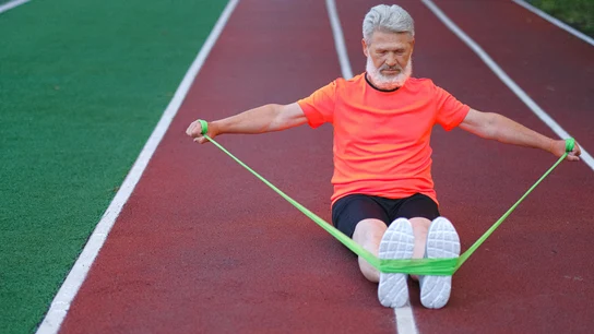 Un hombre se ejercita con una banda elástica sobre una pista de atletismo Un hombre se ejercita con una banda elástica sobre una pista de atletismo