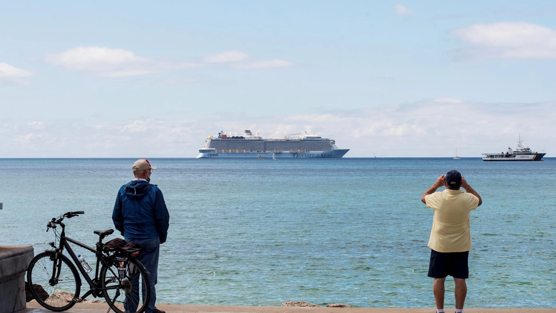 Unos hombres observan un crucero turístico en la bahía de Palma de Mallorca