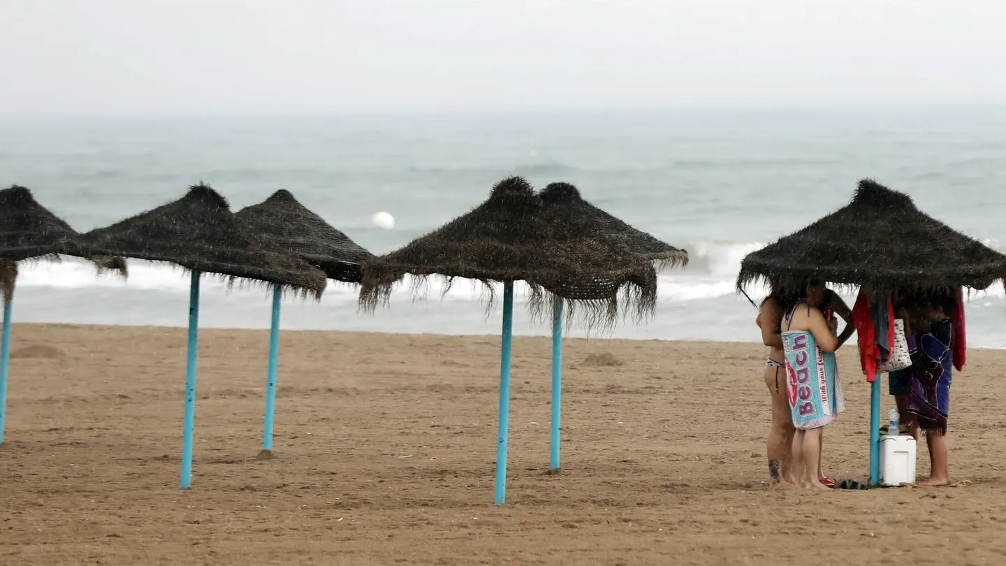 Unos bañistas se protegen de la lluvia bajo una sombrilla Unos bañistas se protegen de la lluvia bajo una sombrilla