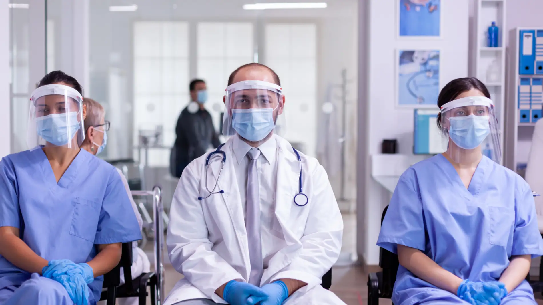 dos enfermeras y un médico sentados y con el equipo de protección