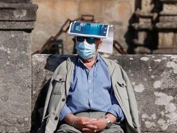 Un hombre se protege del sol con una revista sobre la cabeza en la plaza del Orbadoiro en Santiago de Compostela