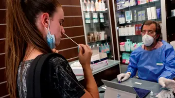 Un farmacéutico explica a una joven cómo realizar un autotest de antígenos en Barcelona