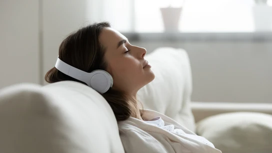 Mujer escucha tranquilamente sus auriculares en el sofá Mujer escucha tranquilamente sus auriculares en el sofá