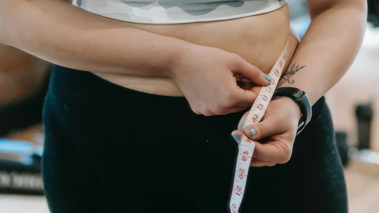 Una mujer midiendo su perímetro abdominal, un factor de riesgo de obesidad Una mujer midiendo su perímetro abdominal, un factor de riesgo de obesidad