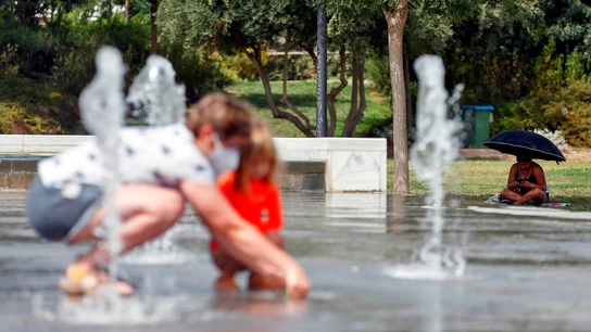 Una mujer se protege del intenso sol bajo un paraguas, mientras otra juega con un niño en una fuente del Parque Central de Valéncia. Una mujer se protege del intenso sol bajo un paraguas, mientras otra juega con un niño en una fuente del Parque Central de Valéncia.