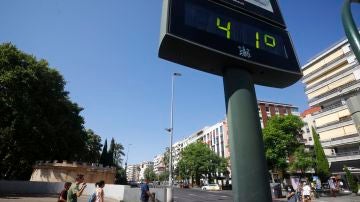 Unas personas caminan por una calle del centro de Córdoba junto a un termómetro que marca 41 grados.