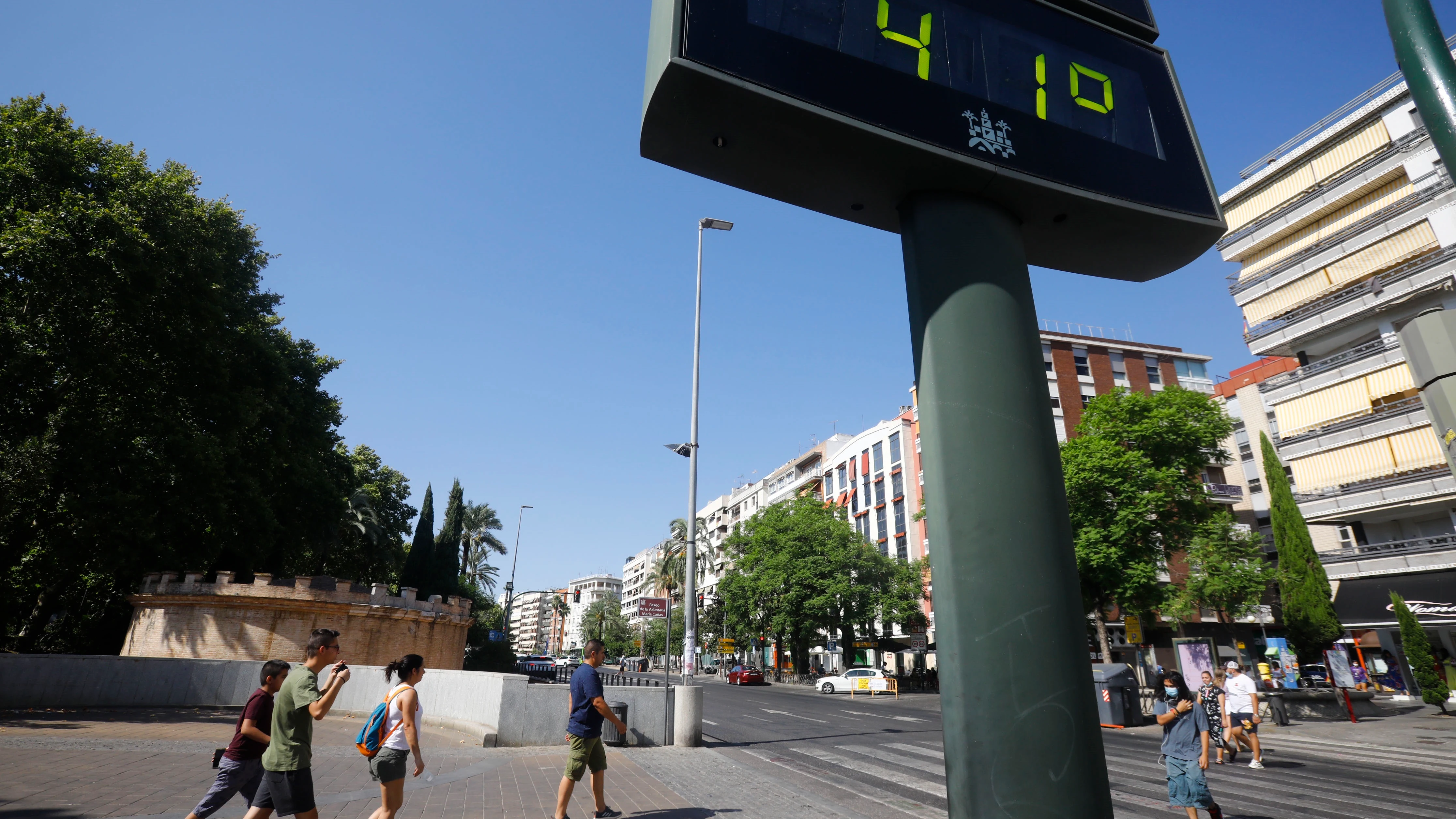 Unas personas caminan por una calle del centro de Córdoba junto a un termómetro que marca 41 grados.