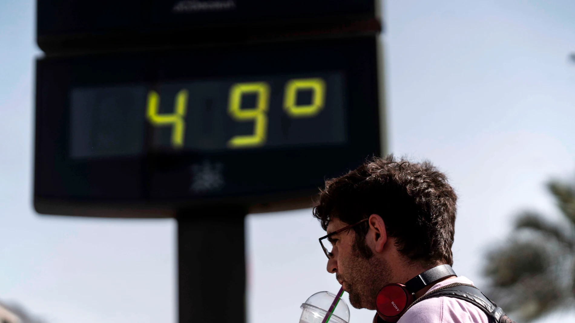 Un hombre toma una bebida junto a un termómetro de Córdoba este sábado