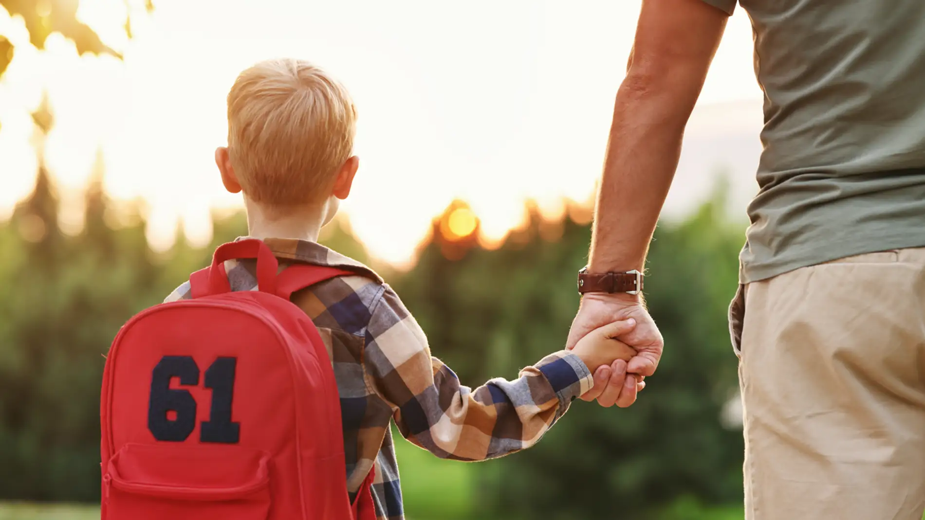 niño con mochila de espaldas y con su padre de la mano 