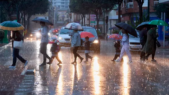 Varias personas cruzan una calle bajo la lluvia Varias personas cruzan una calle bajo la lluvia