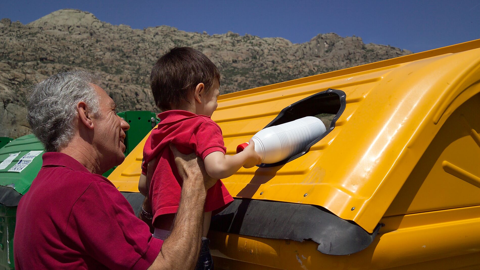 Abuelo y nieto depositando una botella en el contenedor amarillo.