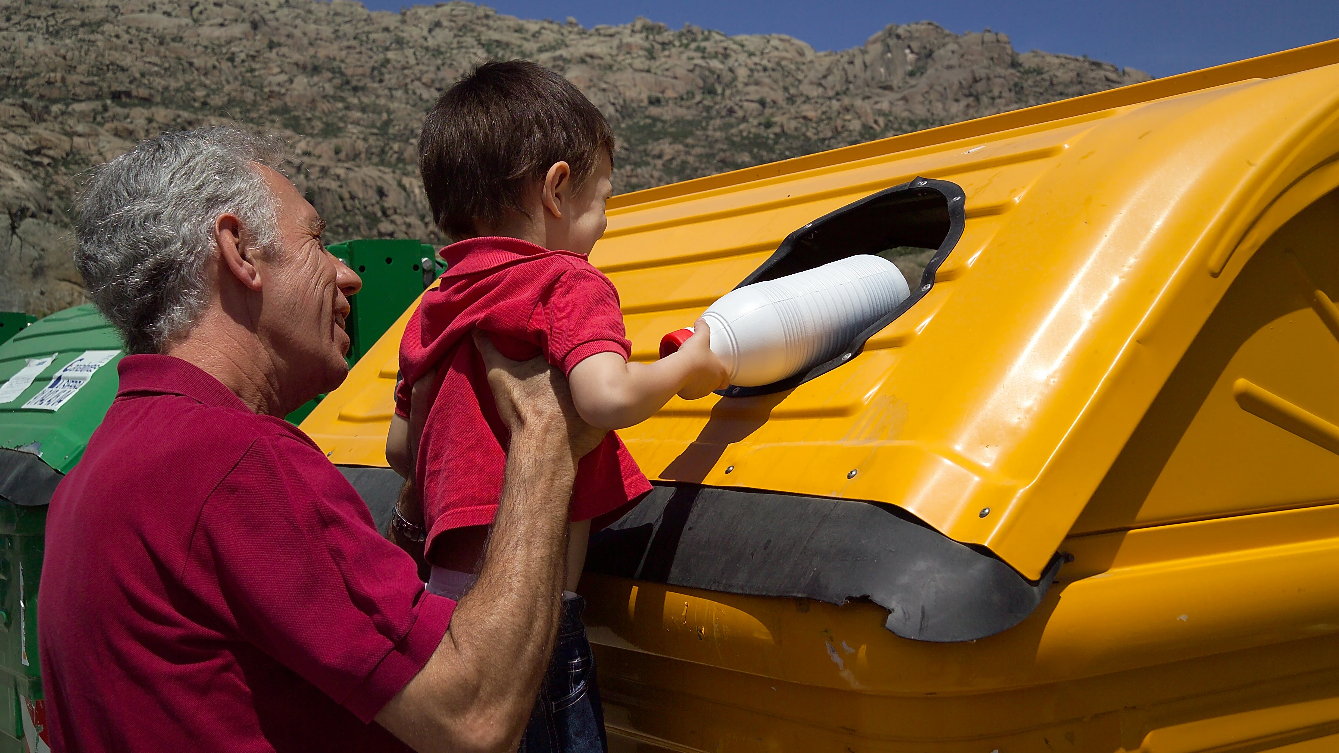 Abuelo y nieto depositando una botella en el contenedor amarillo.