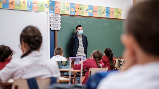 Un profesor da clase con mascarilla a un grupo de niños Un profesor da clase con mascarilla a un grupo de niños