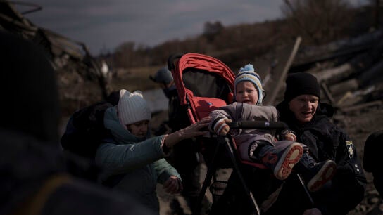 Un ni&ntilde;o es llevado en un cochecito por un camino improvisado mientras huye de Irpin, en las afueras de Kiev
