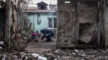 Un hombre enciende un fuego debajo de la tetera en el patio de un edificio de apartamentos afectado por los bombardeos en Mariupol