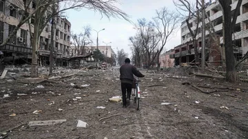 Un hombre camina con una bicicleta por una calle devastada en Mariúpol