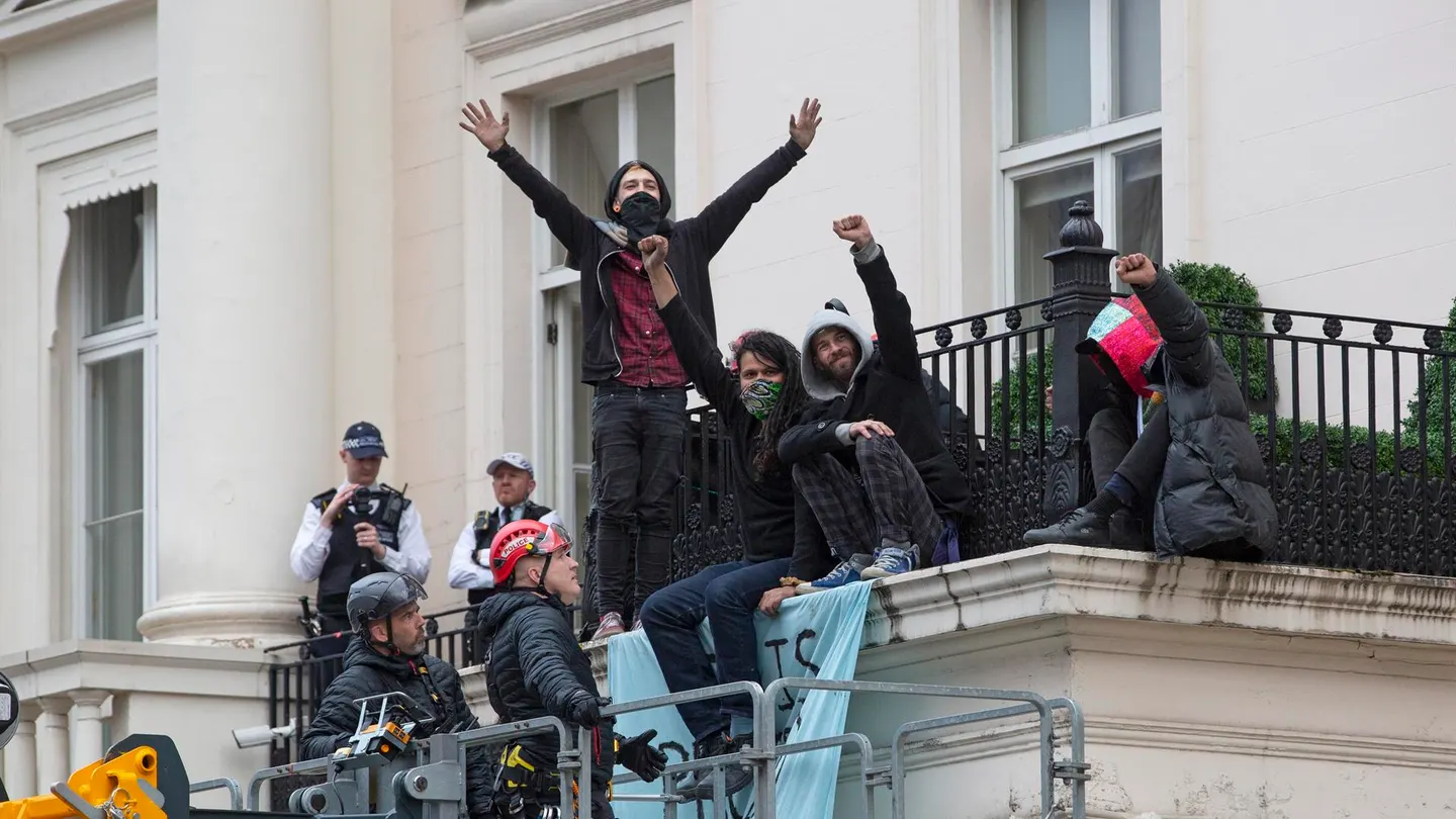 Un grupo de ocupantes ilegales se sienta en el borde de un balcón junto a una pancarta que dice "Esta propiedad ha sido liberada". Un grupo de ocupantes ilegales se sienta en el borde de un balcón junto a una pancarta que dice "Esta propiedad ha sido liberada".