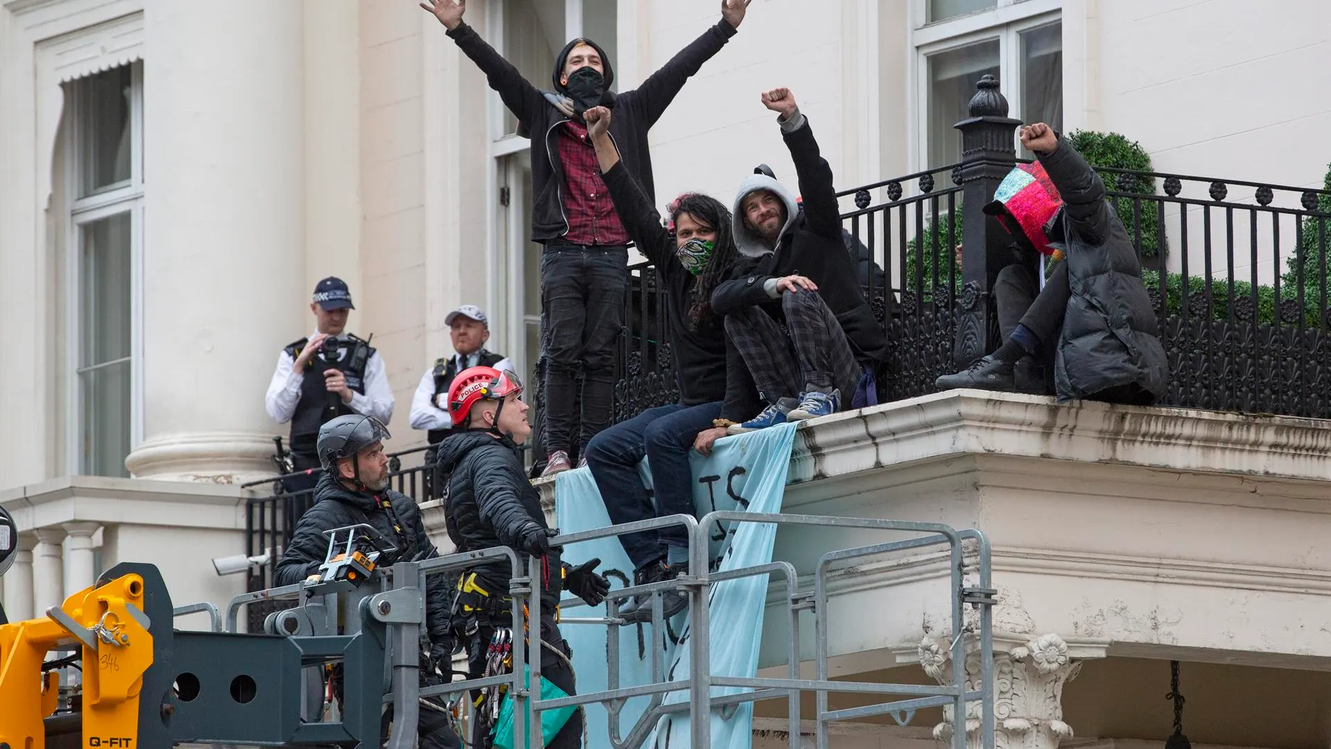  Un grupo de ocupantes ilegales se sienta en el borde de un balcón junto a una pancarta que dice "Esta propiedad ha sido liberada".