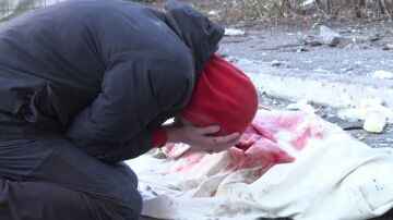 Un hombre llora al lado del cuerpo de su madre, cubierta por una sábana blanca ensangrentada tras un ataque en Kiev