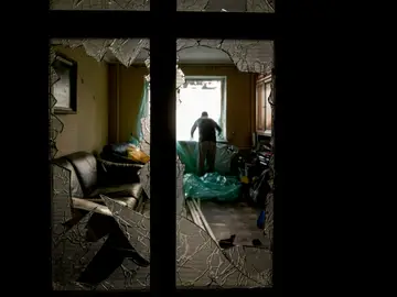 Slava Chikov cubre la ventana rota de su sala de estar con una lámina de plástico en un edificio dañado por un bombardeo el día anterior en Kiev, Ucrania