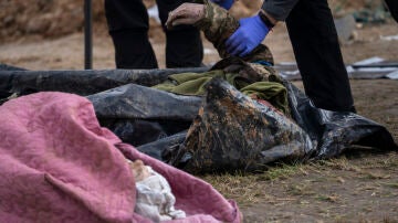 Un policía examina el cadáver de un soldado ucraniano tras sacarlo de una fosa común en Bucha.