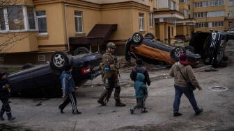 Ni&ntilde;os y soldados frente a coches destrozados en Bucha, Ucrania