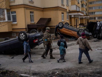 Ni&ntilde;os y soldados frente a coches destrozados en Bucha, Ucrania