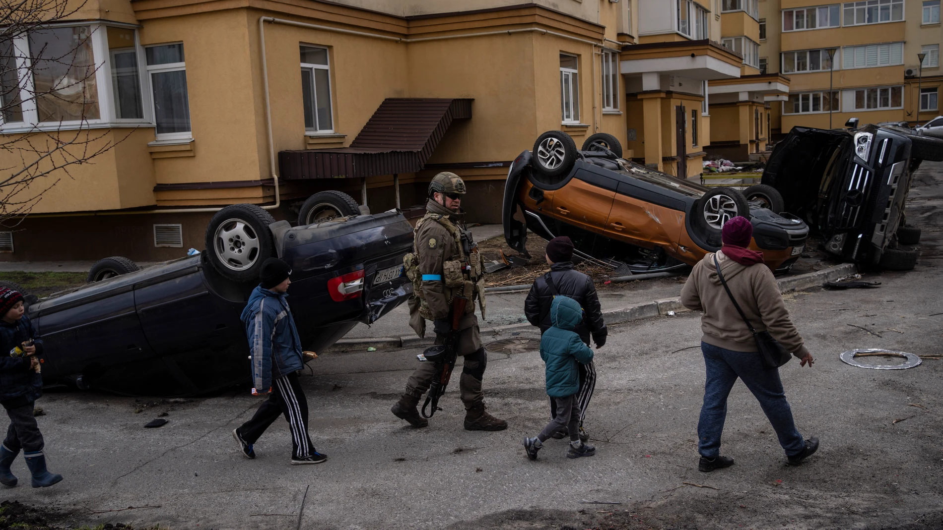 Niños y soldados frente a coches destrozados en Bucha, Ucrania