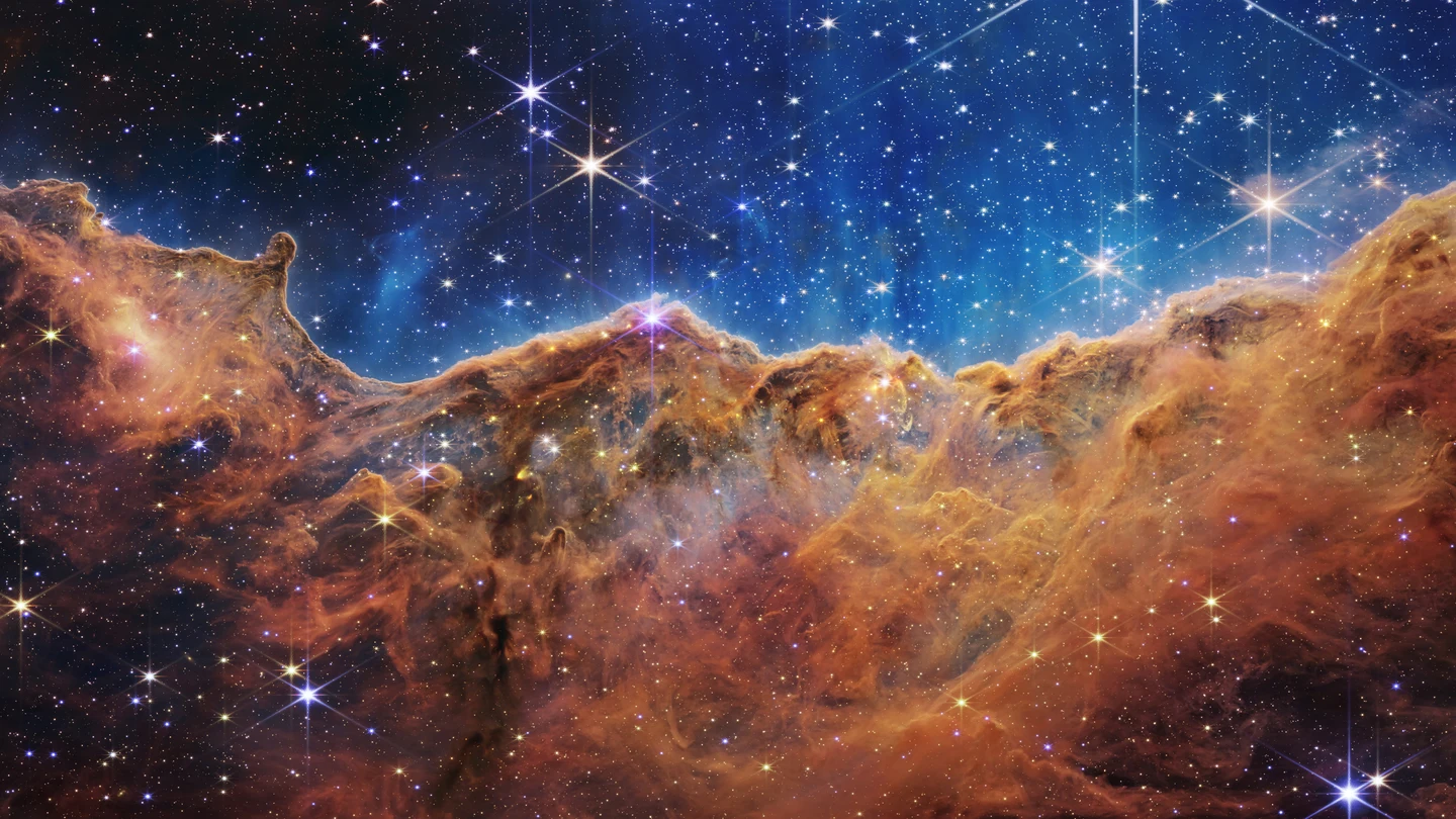 Imagen del borde de una región cercana y joven donde se forman estrellas, llamada NGC 3324, en la Nebulosa de Carina, que se asemeja a un paisaje de "montañas" y "valles" salpicados de estrellas brillantes. Imagen del borde de una región cercana y joven donde se forman estrellas, llamada NGC 3324, en la Nebulosa de Carina, que se asemeja a un paisaje de "montañas" y "valles" salpicados de estrellas brillantes.