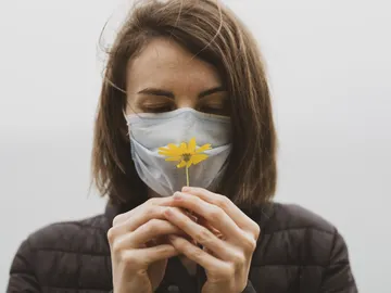 Mujer con mascarilla oliendo una flor Mujer con mascarilla oliendo una flor