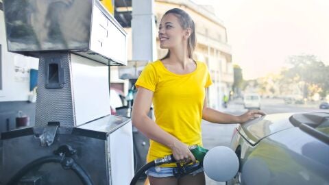 Mujer joven sonríe mientras pone gasolina al coche