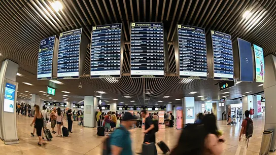 Varios pasajeros pasan por las pantallas de información en el aeropuerto Adolfo Suárez Madrid-Barajas. Nueva huelga en Ryanair: todos los días afectados en el mes de agosto