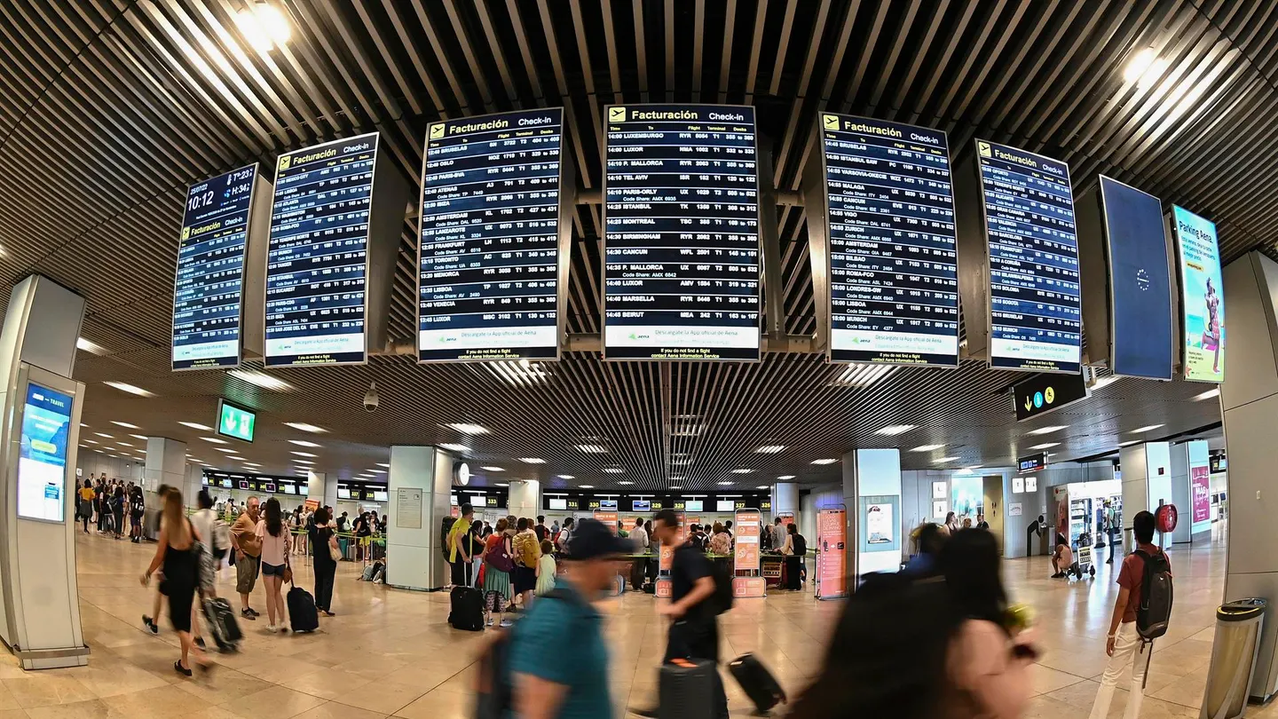 Varios pasajeros pasan por las pantallas de información en el aeropuerto Adolfo Suárez Madrid-Barajas. Nueva huelga en Ryanair: todos los días afectados en el mes de agosto