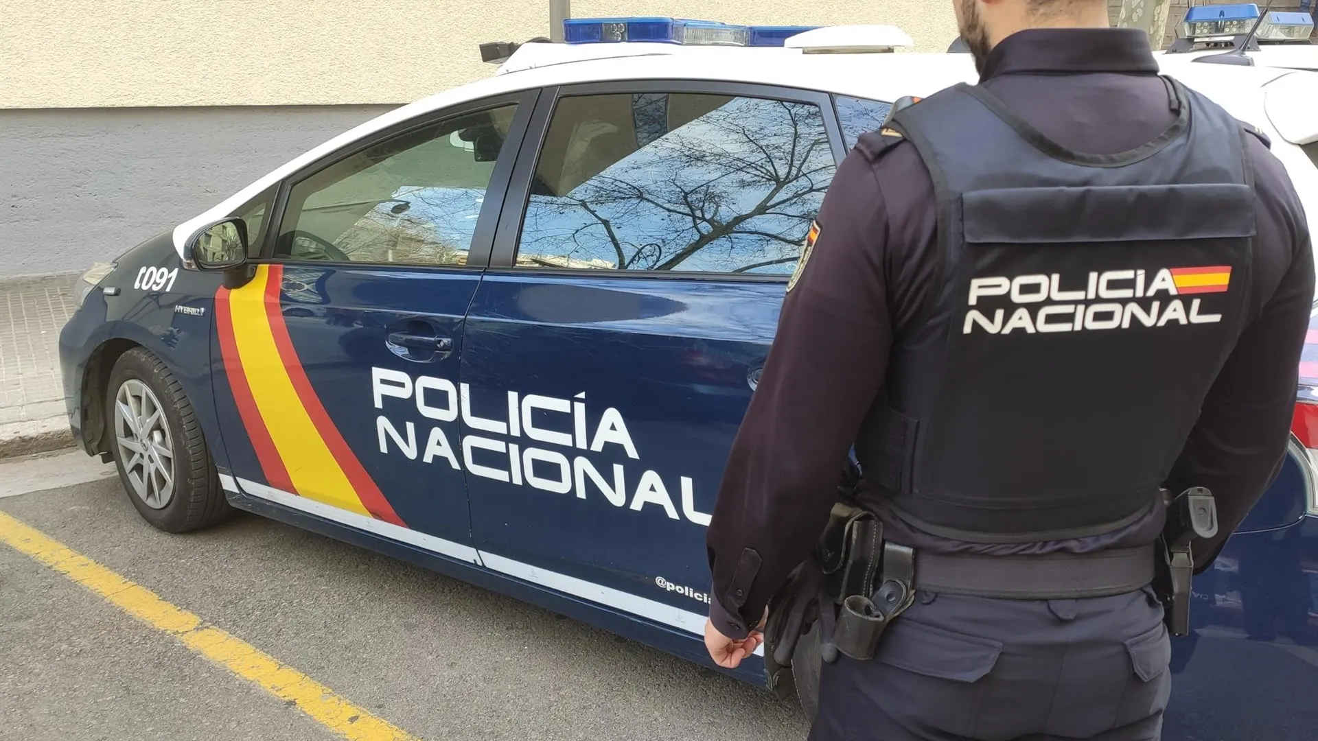 Un agente de la Policía Nacional en Palma junto al coche policial.