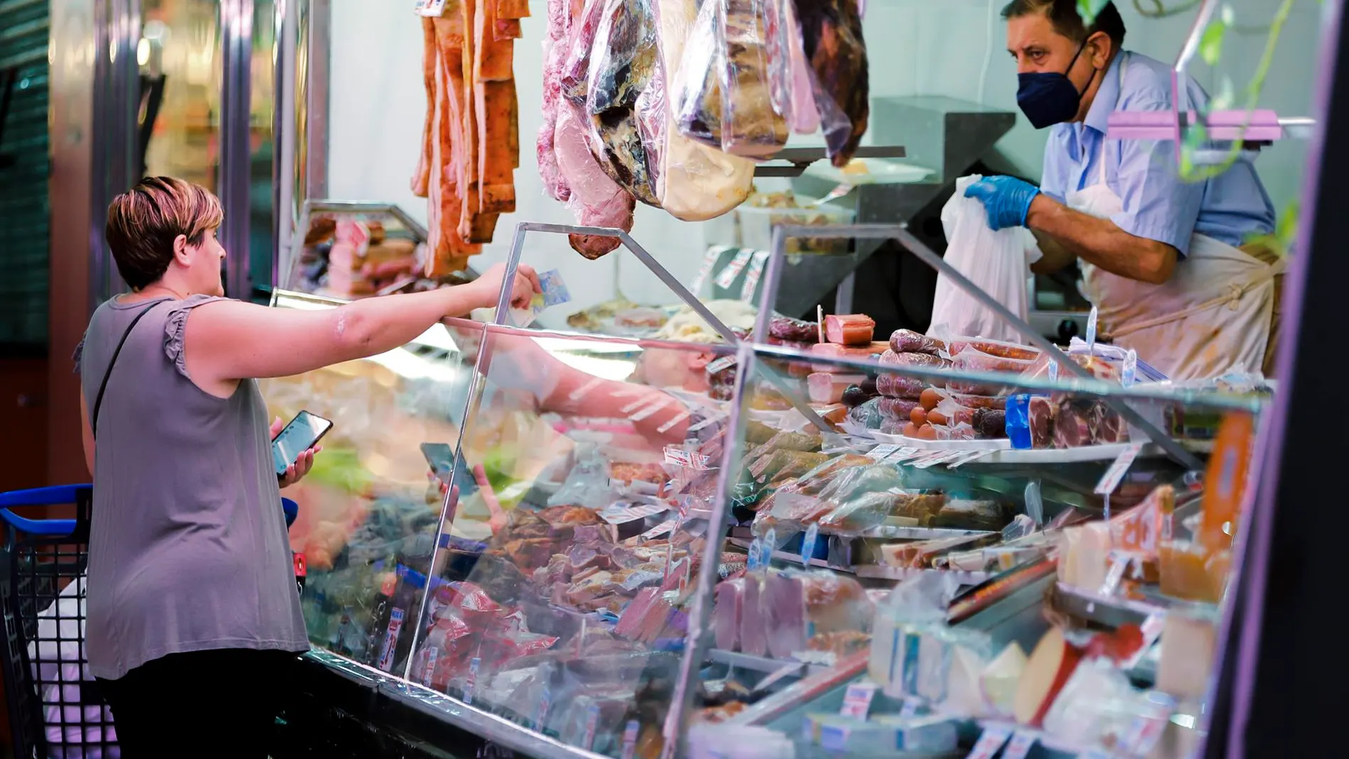 Una mujer compra en un puesto de charcutería de un mercado de Madrid, en julio