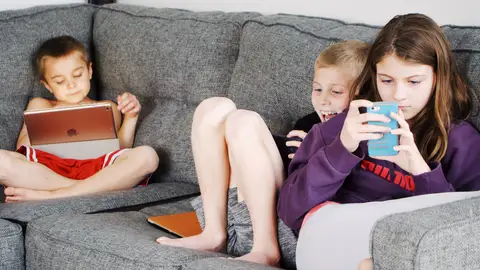 Tres niños en el sofá mirando la tablet y el teléfono móvil. Tres niños en el sofá mirando la tablet y el teléfono móvil.