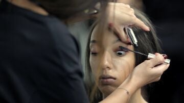 Una maquilladora maquilla a una modelo en el backstage de un desfile.