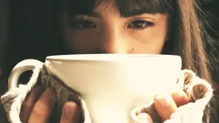 Una chica triste bebiendo de una taza. 