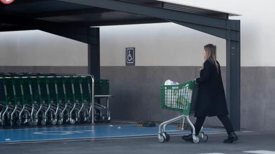 Una mujer sale de un supermercado con un carro de la compra. Una mujer sale de un supermercado con un carro de la compra.