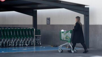 Una mujer sale de un supermercado con un carro de la compra.