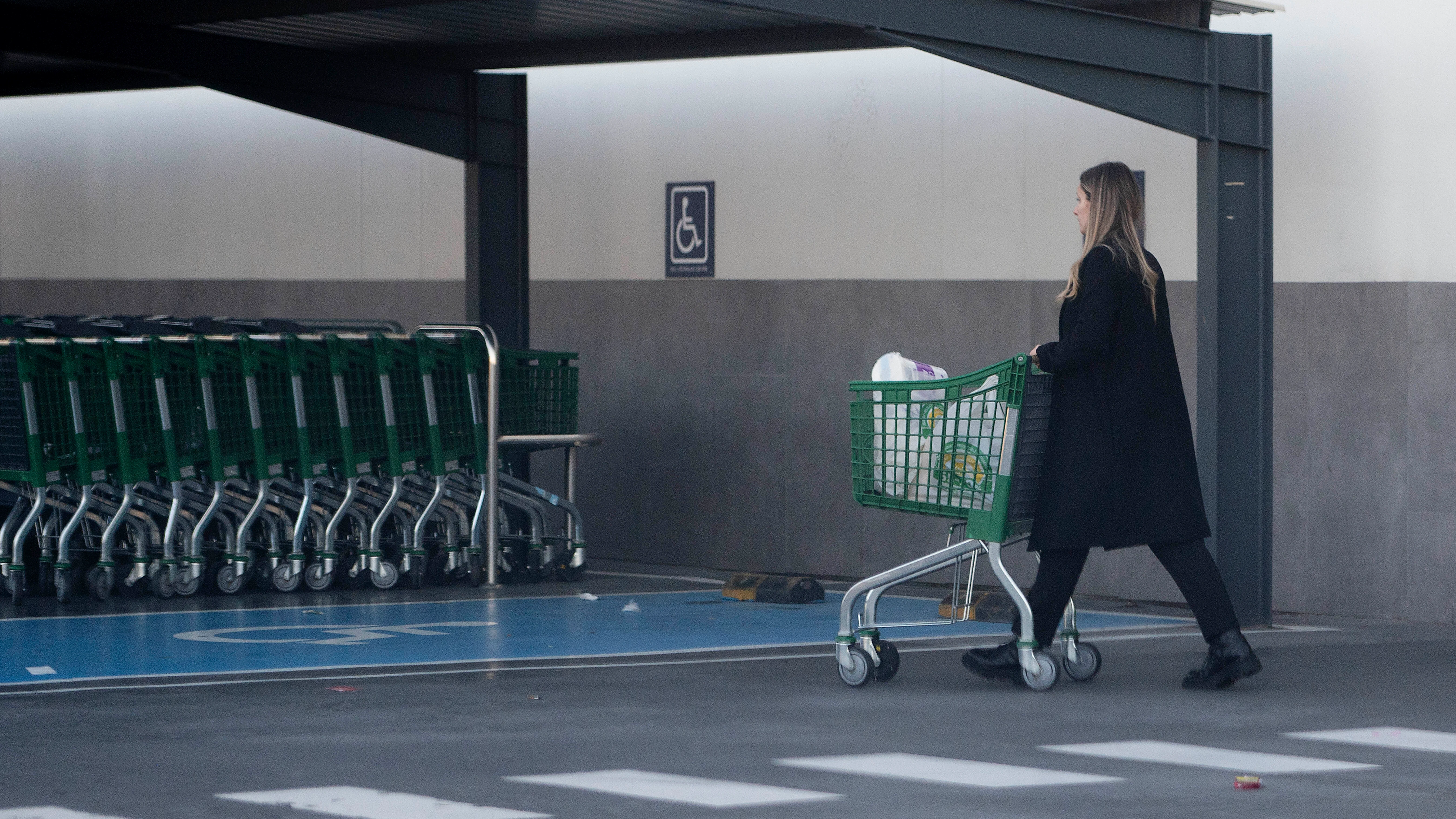 Una mujer sale de un supermercado con un carro de la compra.