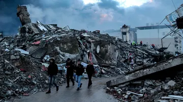 Gente caminando junto a los escombros de un edificio colapsado en Hatay. 