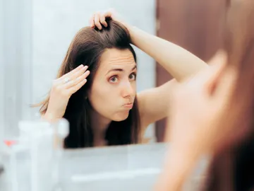 Chica mirándose el pelo en el espejo haciendo una mueca Chica mirándose el pelo en el espejo haciendo una mueca