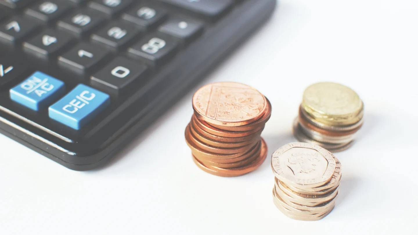 Una calculadora y unas monedas sobre un escritorio. Cómo funcionan los tramos del IRPF y cómo afectan a tu nómina