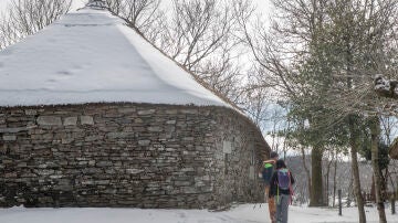 Dos peregrinos pasean cerca de una palloza cubierta por la nieve en el pueblo de O Cebreiro, Lugo