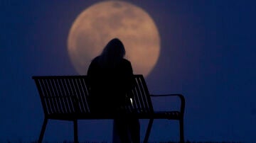 Una mujer sentada en un banco mirando la luna llena de abril de 2021 en New Albany (Indianapolis, Estados Unidos)
