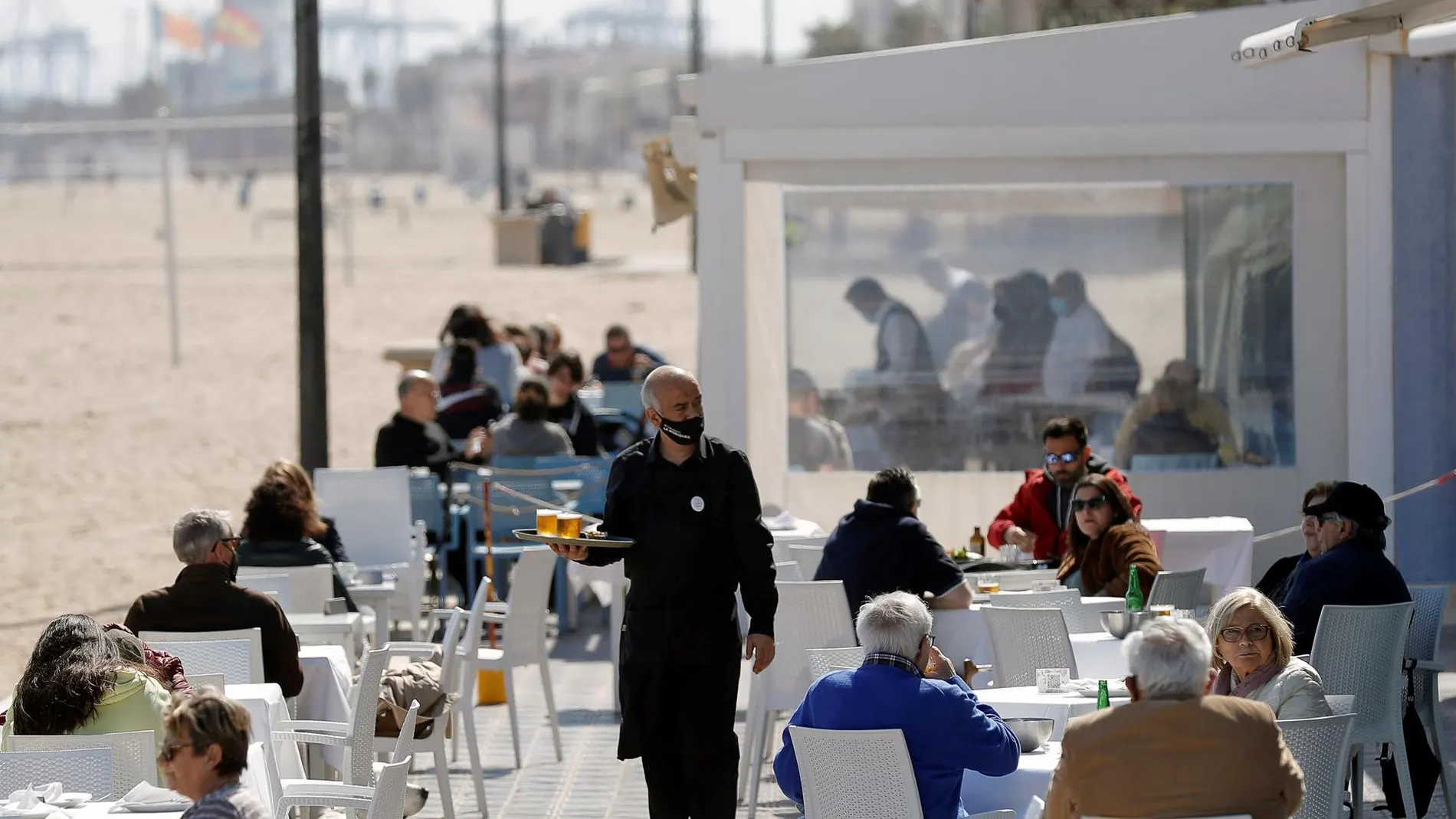 Un camarero atiende las mesas de una terraza en uno de los restaurantes de la playa de la playa de la Malvarrosa de Valencia